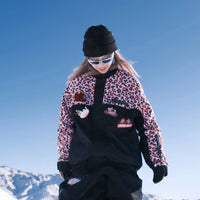 Person in leopard print jacket and black pants standing on a snowy slope with a clear blue sky.