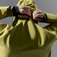 Person wearing a light green jacket with tattoos on arms against a gray background