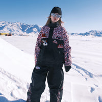 Person in winter clothing standing on a snowy landscape with mountains in the background