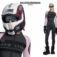 Person wearing a black and pink snow sports outfit with helmet and goggles on a white background.
