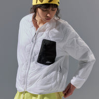 Person wearing a white jacket with a black pocket and yellow pants, standing against a gray background.