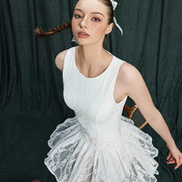 Woman in a white lace dress sitting against a dark curtain