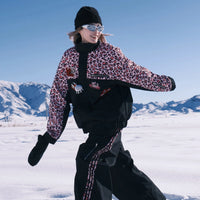 Person in leopard print jacket and black pants standing on snow with mountains in the background
