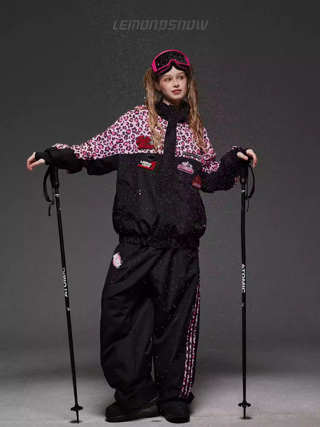 Person wearing a black and red ski outfit with goggles, holding ski poles on a gray background.