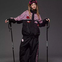 Person wearing a black and red ski outfit with goggles, holding ski poles on a gray background.
