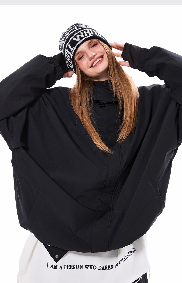 Person wearing a black oversized jacket and a beanie with text, standing against a white background