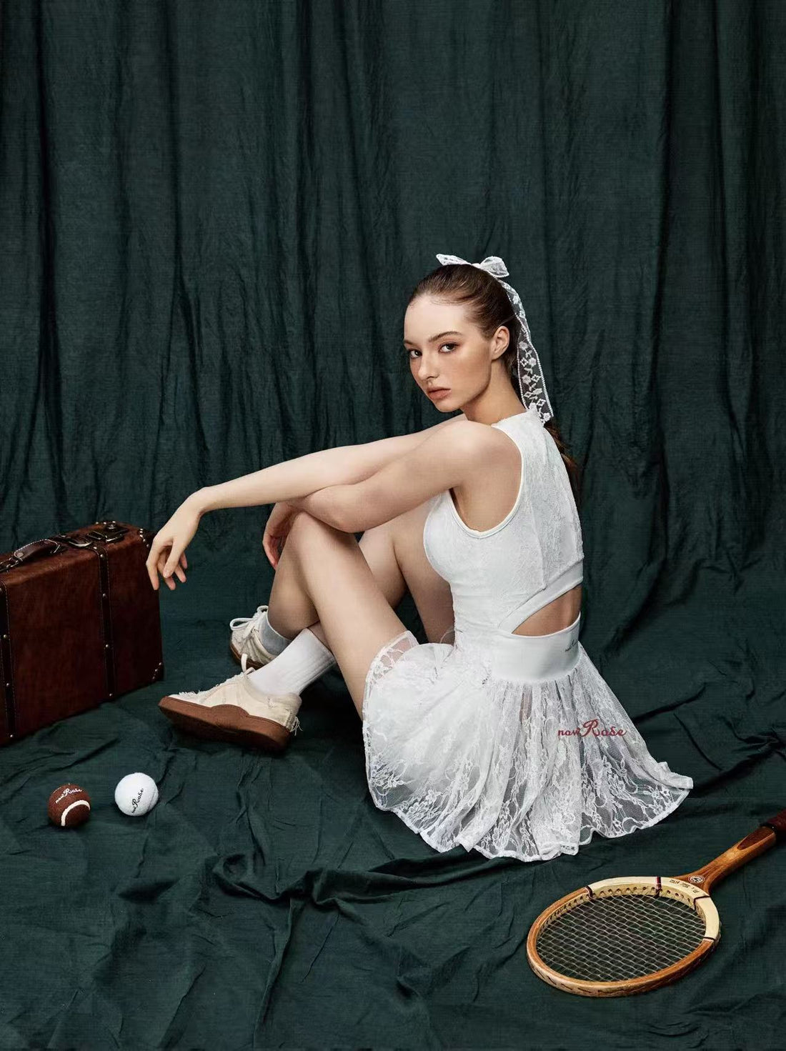 Woman in a white dress sitting on a green fabric background with sports equipment around.