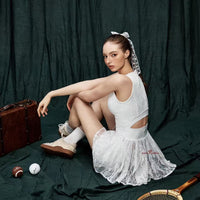 Woman in a white dress sitting on a green fabric background with sports equipment around.