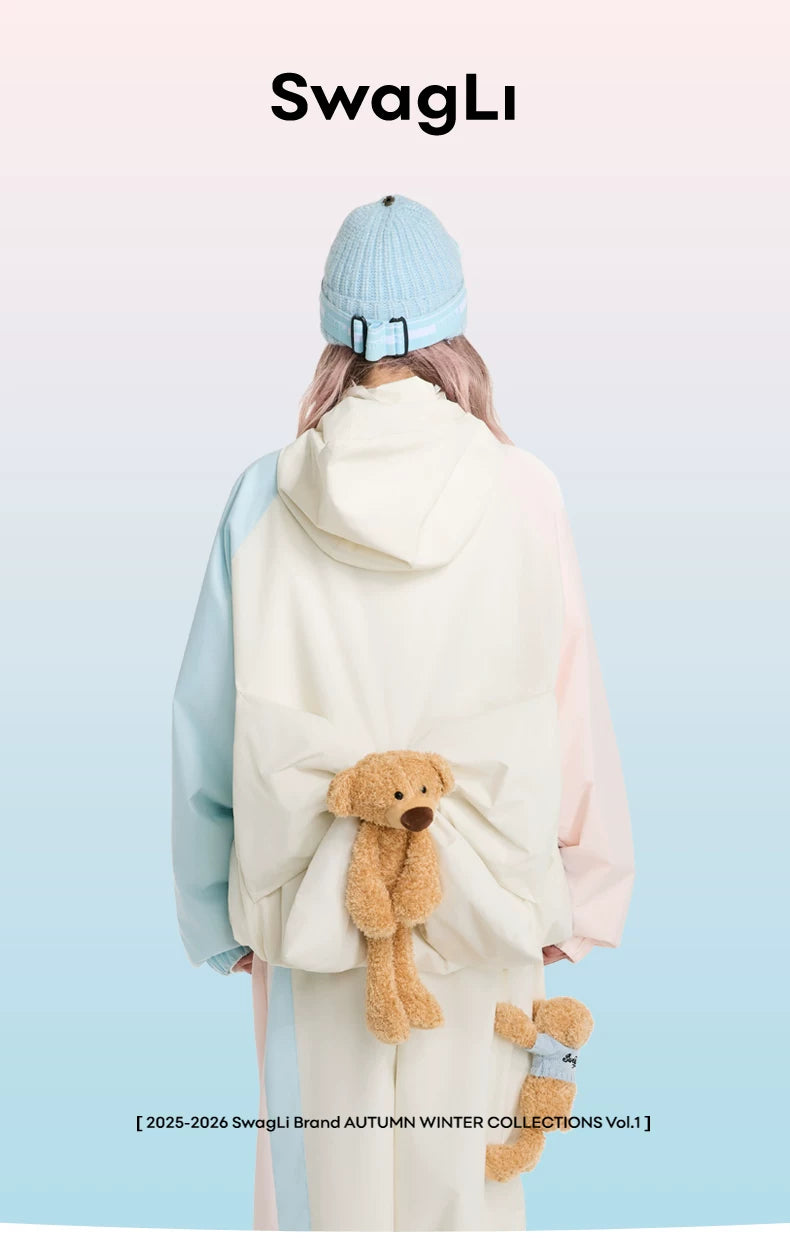 Person wearing a light blue beanie and white coat with teddy bear design, holding teddy bear, on a light blue background with &