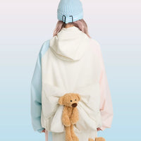 Person wearing a light blue beanie and white coat with teddy bear design, holding teddy bear, on a light blue background with 'SwagLi' branding.