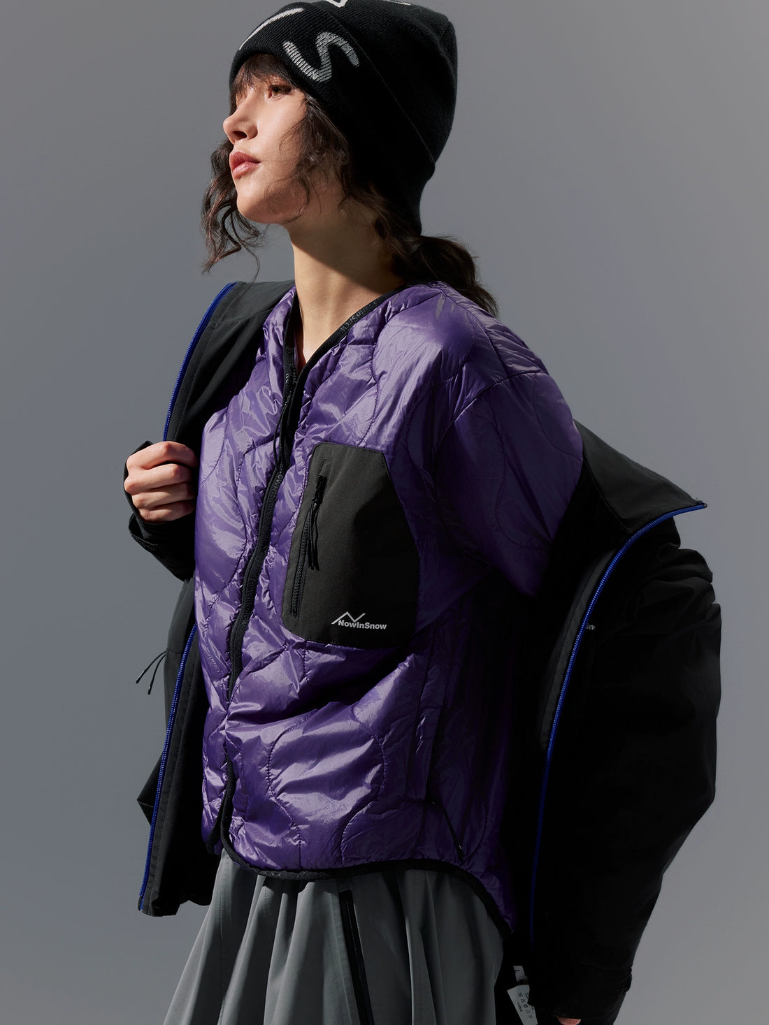 Person wearing a purple jacket with a black backpack against a gray background