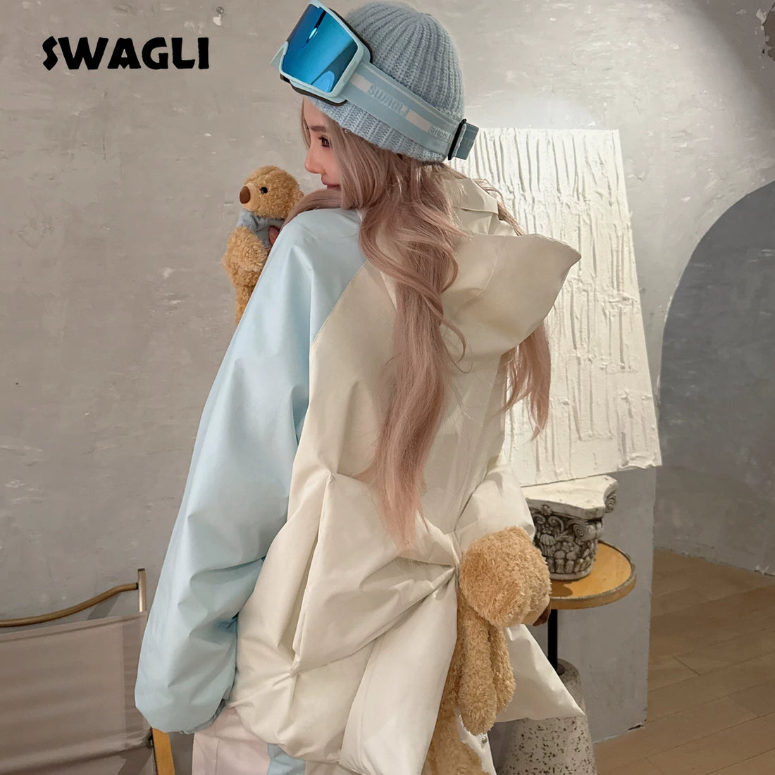 Person wearing a light-colored jacket with fluffy texture, holding a teddy bear, in a room with a neutral color scheme.