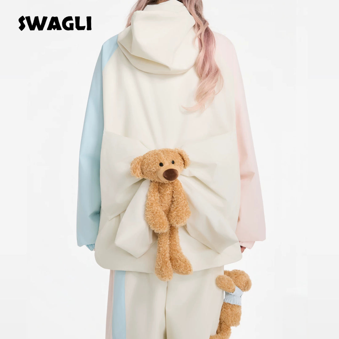 Person wearing a pastel-colored outfit with a teddy bear plush toy, branded &