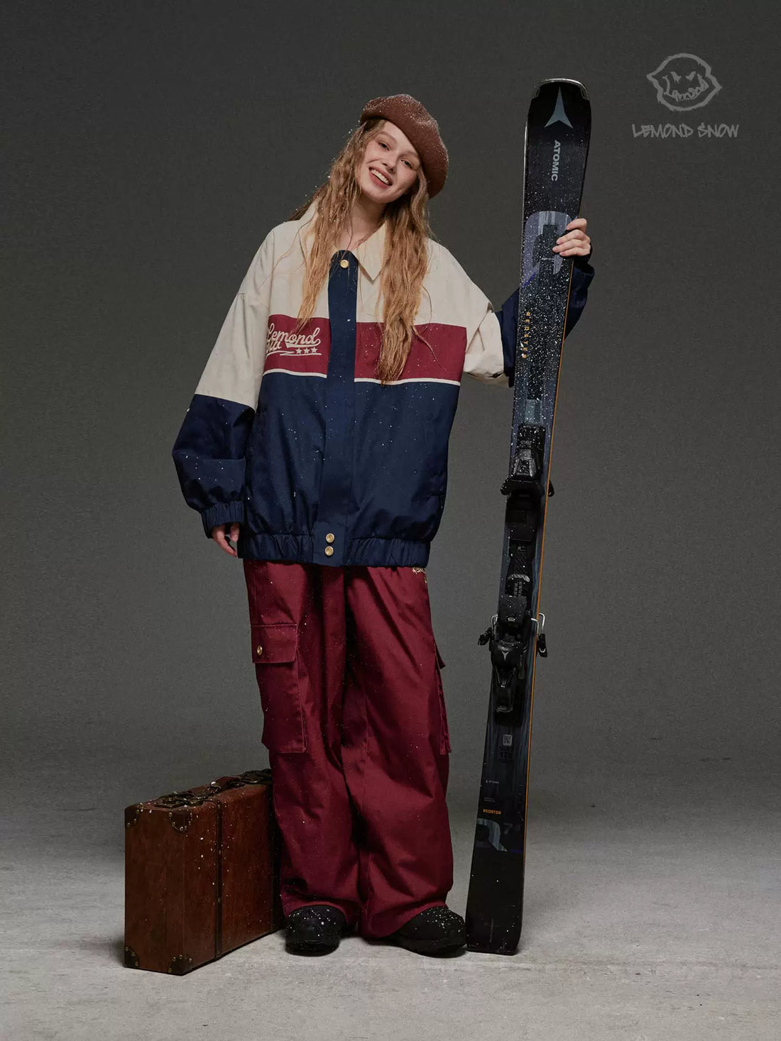 Person wearing a vintage-style ski outfit holding skis against a gray background