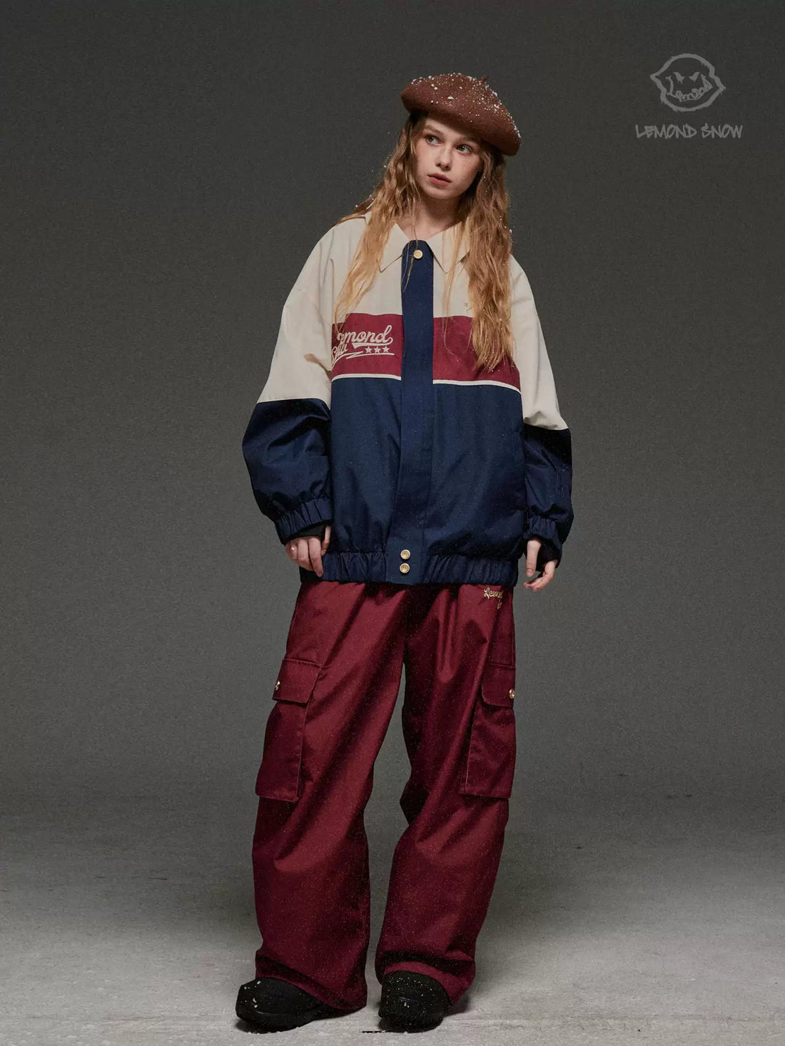 Person wearing a colorful jacket and maroon pants on a gray background