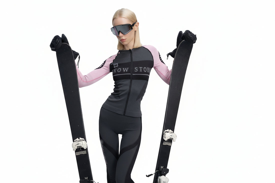 Person wearing a black and pink baselayer with skis, standing against a white background.