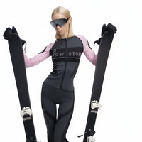 Person wearing a black and pink baselayer with skis, standing against a white background.