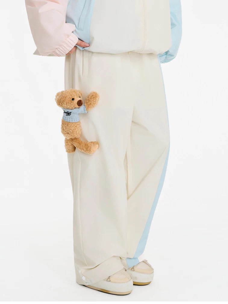 Person wearing a light blue jacket and cream pants holding a small teddy bear with a blue scarf.
