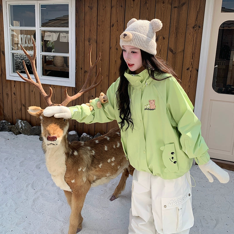 Person in a green jacket and white pants interacting with a deer in a snowy setting.