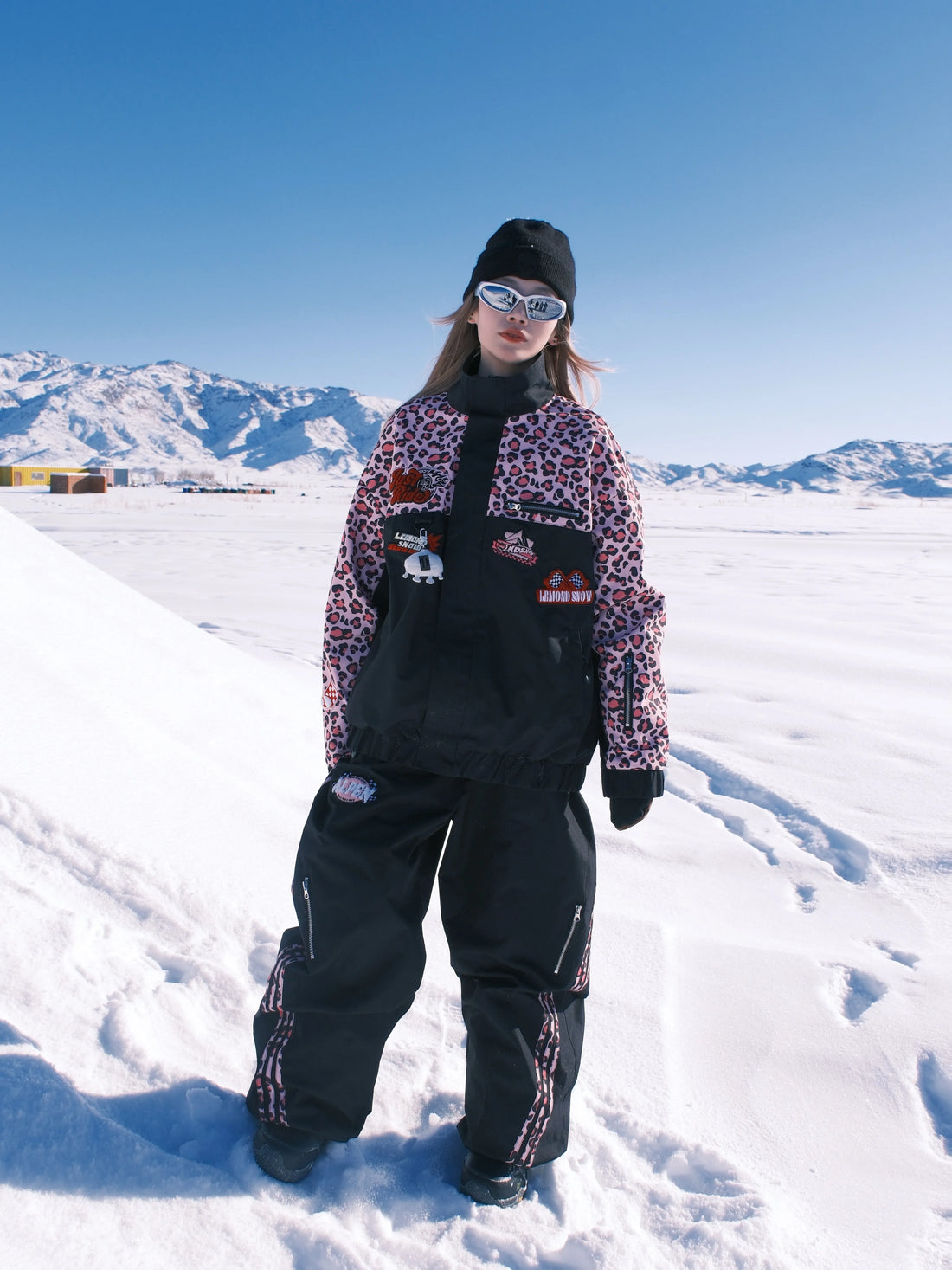 Person in winter clothing standing on a snowy landscape with mountains in the background