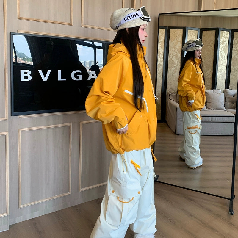 Person wearing a yellow jacket and white pants standing in a room with a mirror and television.