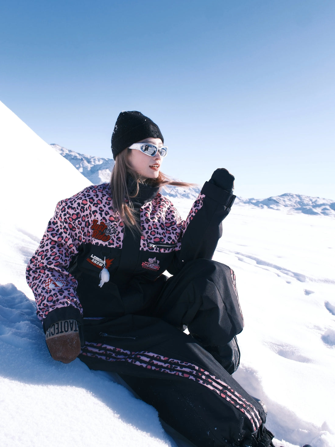 Person sitting on a snowy slope wearing a leopard print jacket and black pants.