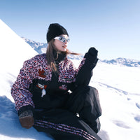 Person sitting on a snowy slope wearing a leopard print jacket and black pants.