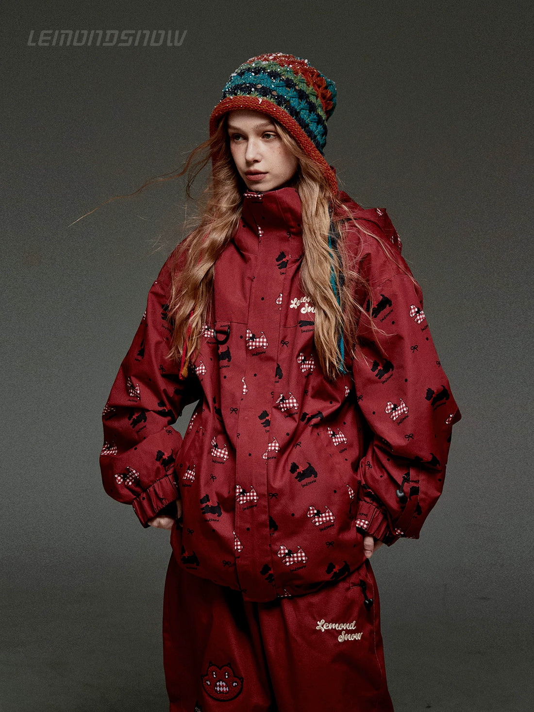 Person wearing a red snowsuit with a pattern, standing against a dark background.