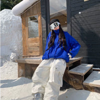 Person in blue jacket and white pants sitting on a wooden bench outside a snow-covered cabin.