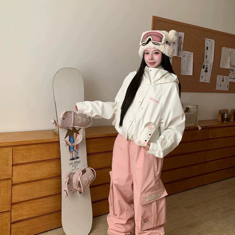 Person in pink and white winter clothing holding a snowboard in a room with wooden furniture.