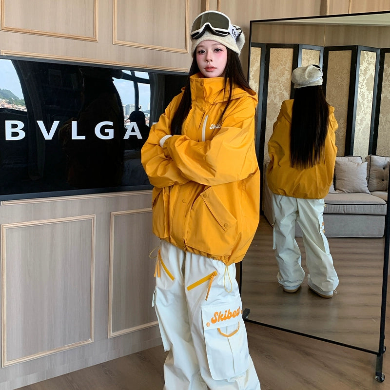 Person wearing a yellow snowboarding jacket and white pants standing in front of a mirror, with a BVLGA logo visible.
