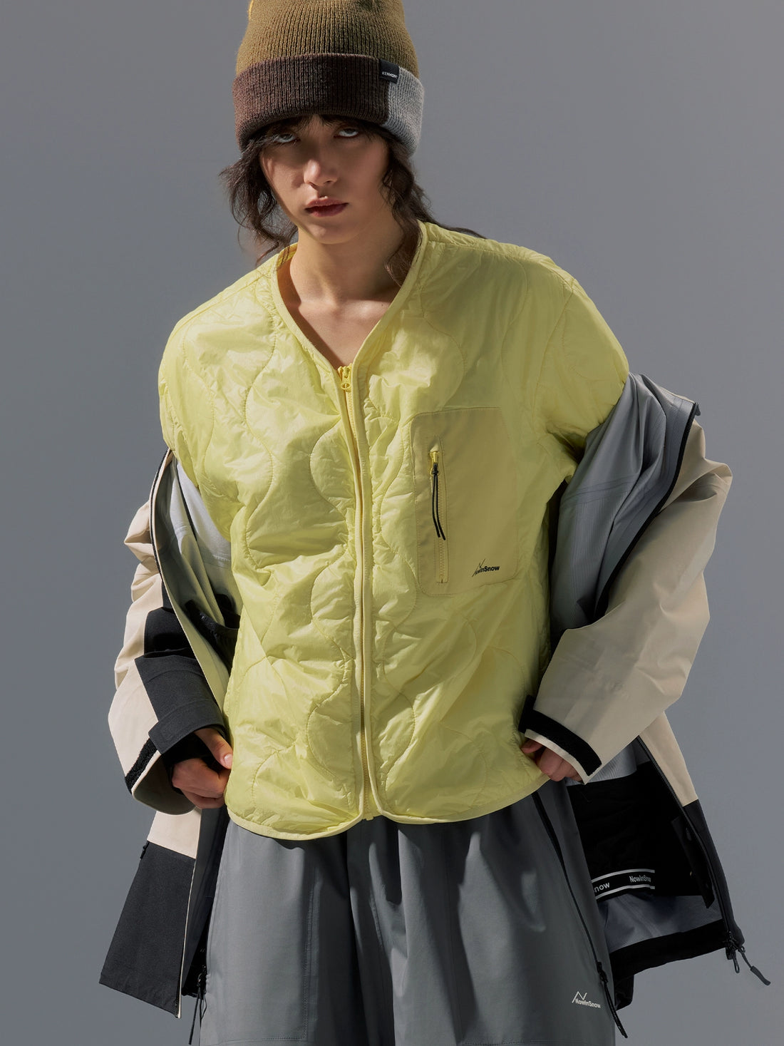 Person wearing a bright yellow jacket and holding bags against a gray background