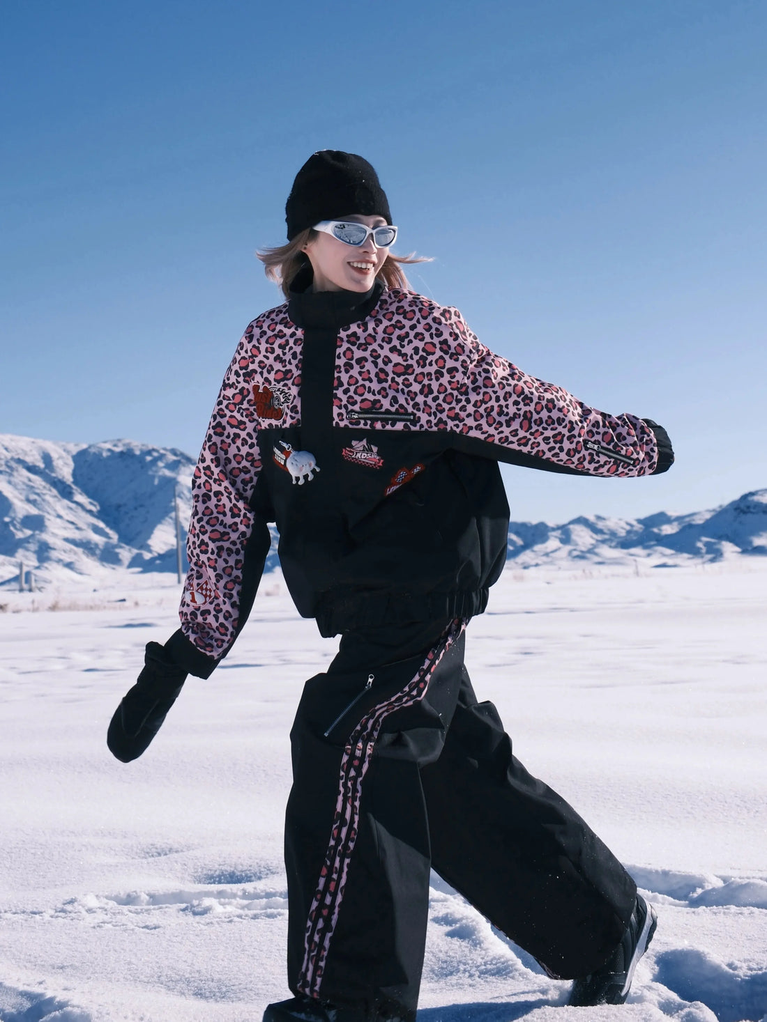 Person in leopard print jacket and black pants standing on snow with mountains in the background