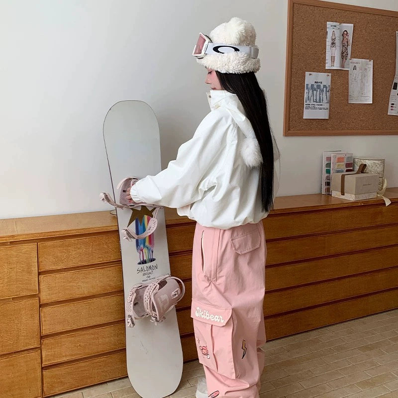 Person in white jacket and pink pants holding a snowboard.