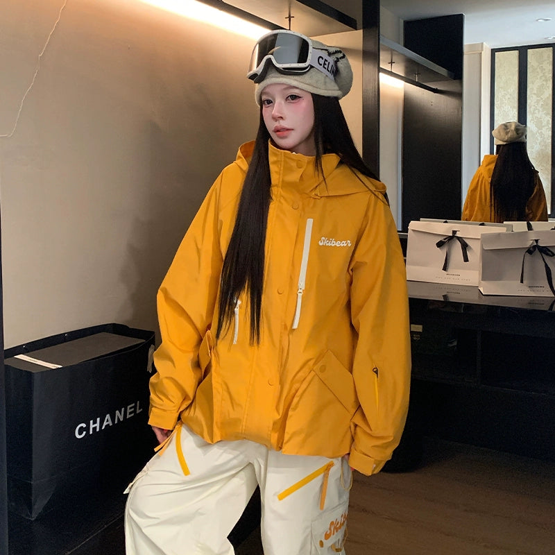 Person wearing a yellow jacket with a brand logo, standing in a room with a Chanel bag.