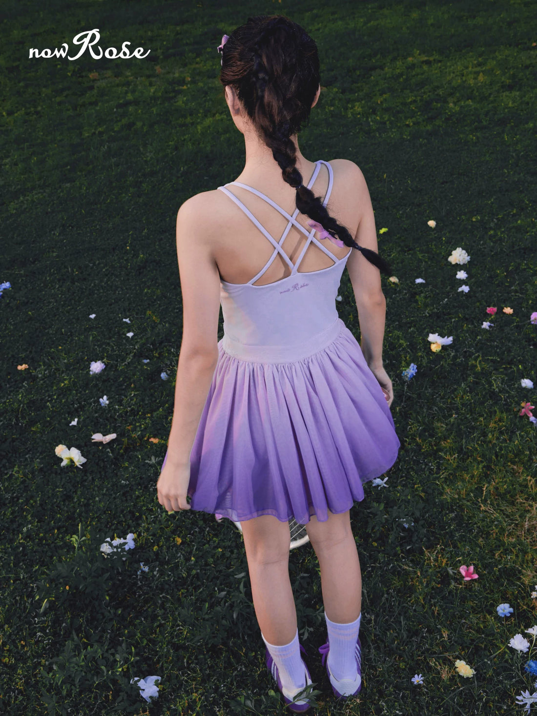 Person wearing a purple dress standing in a grassy area with flowers