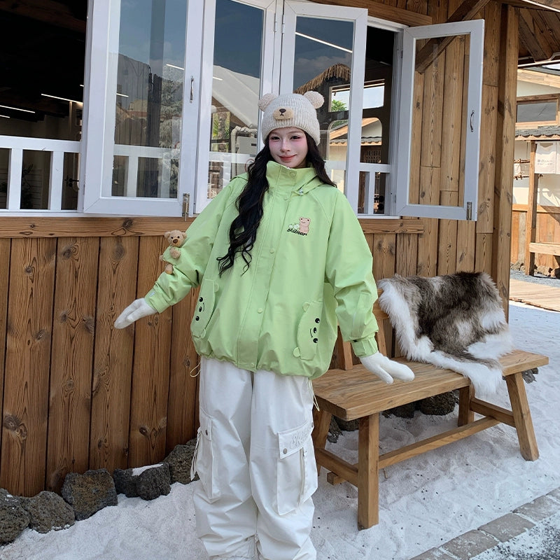 Person wearing a bright green jacket and white pants standing in front of a wooden cabin.