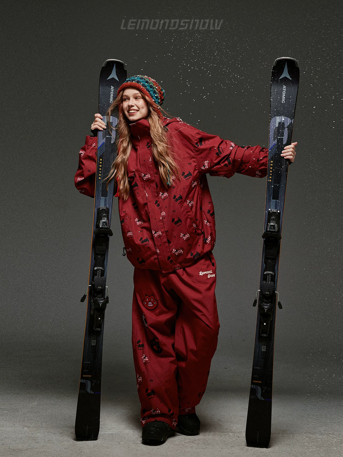 Person in a red ski outfit holding skis against a gray background