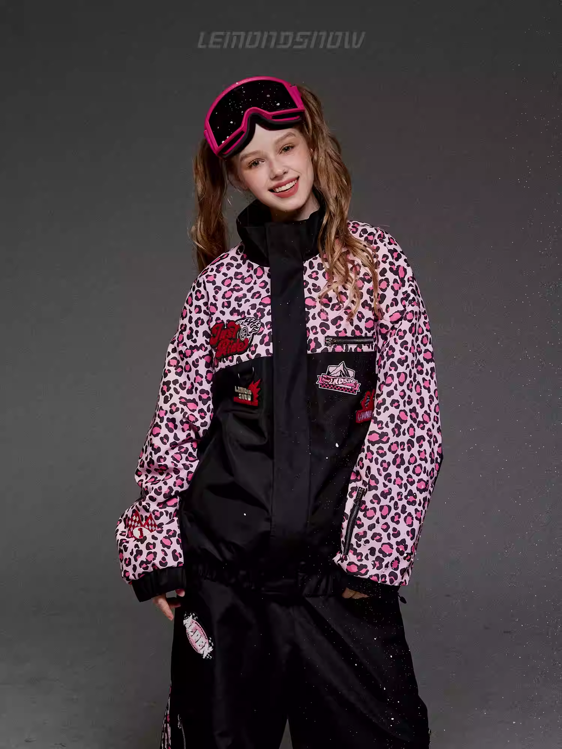 Child wearing a leopard print jacket and black pants with goggles on a gray background