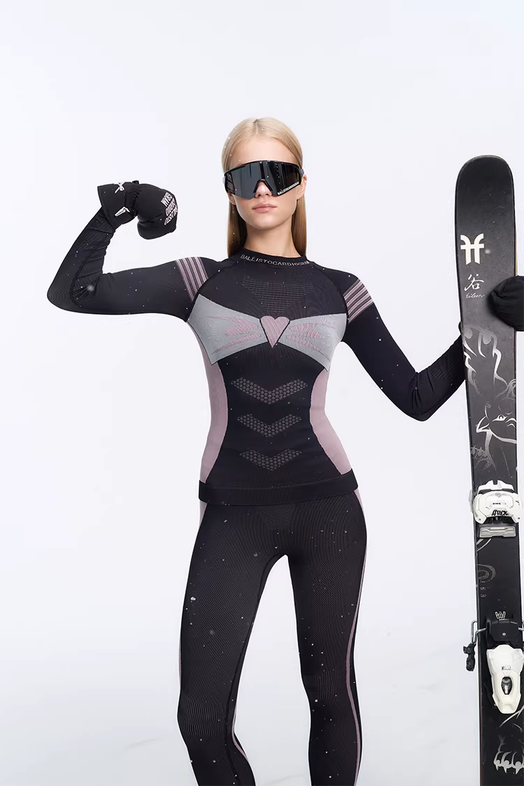 Person wearing a black and gray ski suit with goggles and gloves, holding a ski.
